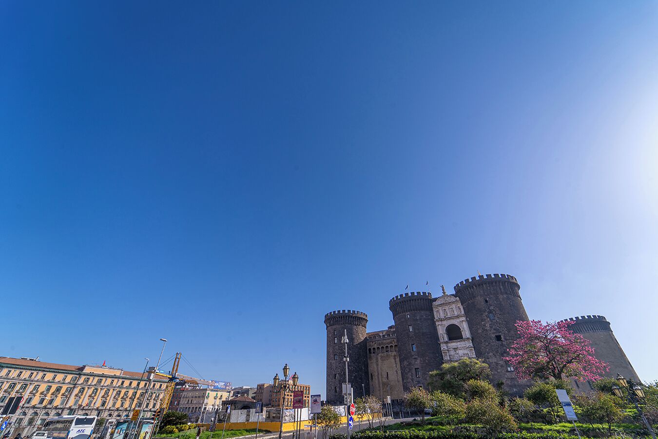 A historic castle with two prominent towers, surrounded by urban buildings and a clear sky.