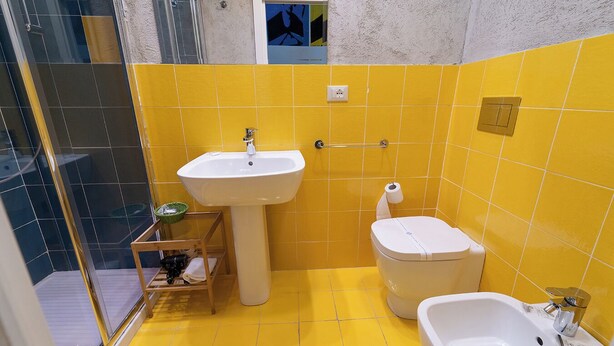 A bathroom with yellow tiles, a white sink, a toilet, and a bidet. - P.C. BOUTIQUE H. CASTEL NUOVO by ClaPa Group Dislocated Hospitality (Naples)