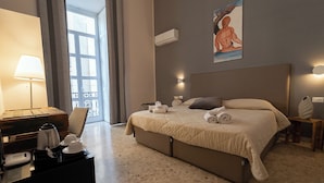 A hotel room with a bed, a desk with a lamp, a painting on the wall, and a window with curtains. - P.C. BOUTIQUE H. CASTEL NUOVO by ClaPa Group Dislocated Hospitality (Naples)
