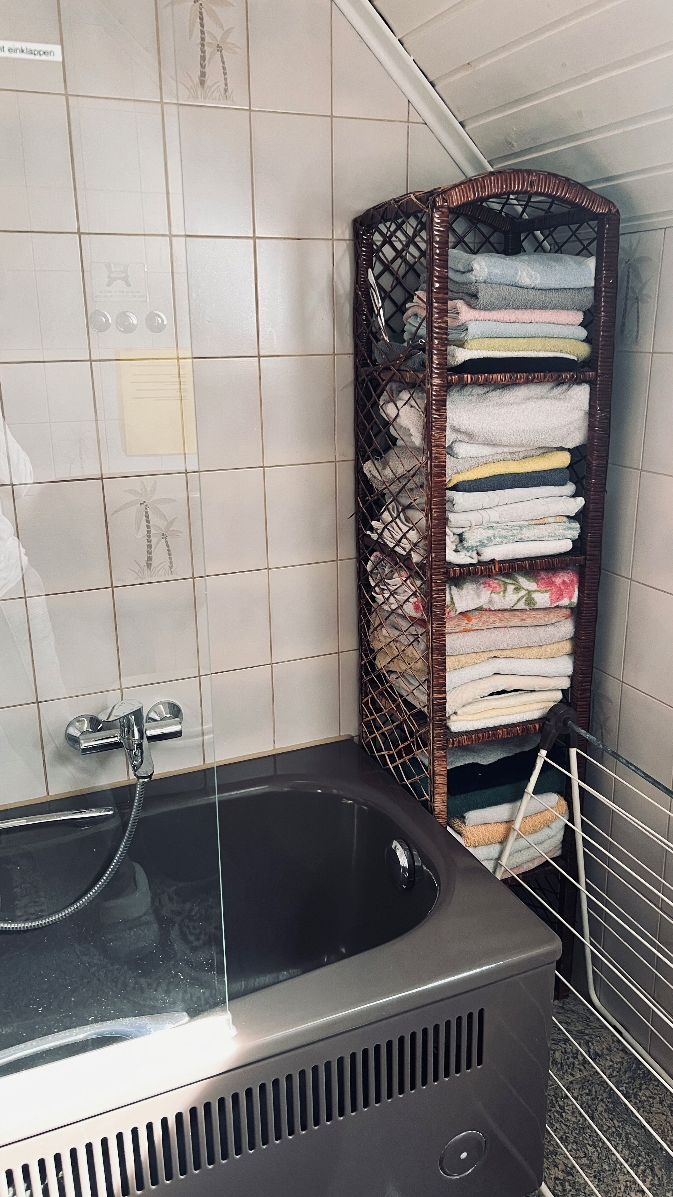 A bathroom with a black bathtub, a metal rack with towels, and a tiled wall.