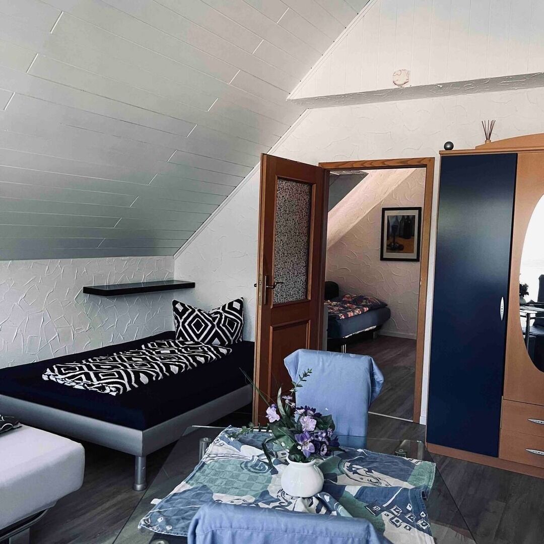 A compact room with a bed, a small table with a vase, and a wardrobe.