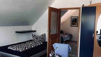 A compact room with a bed, a small table with a vase, and a wardrobe.