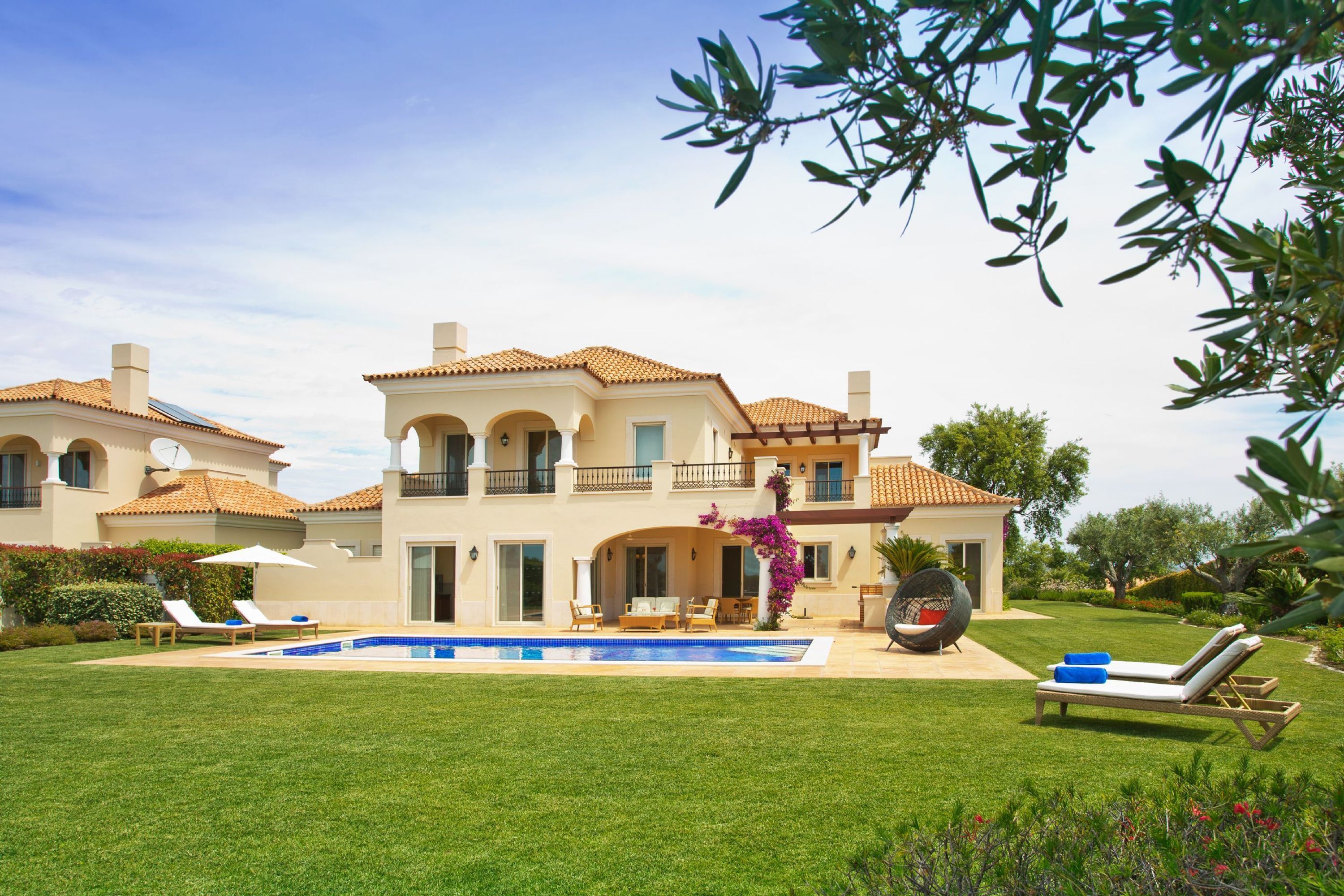A large, two-story house with a swimming pool, multiple lounge chairs, and a well-maintained lawn.