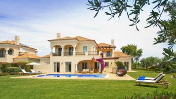 A large, two-story house with a swimming pool, multiple lounge chairs, and a well-maintained lawn.