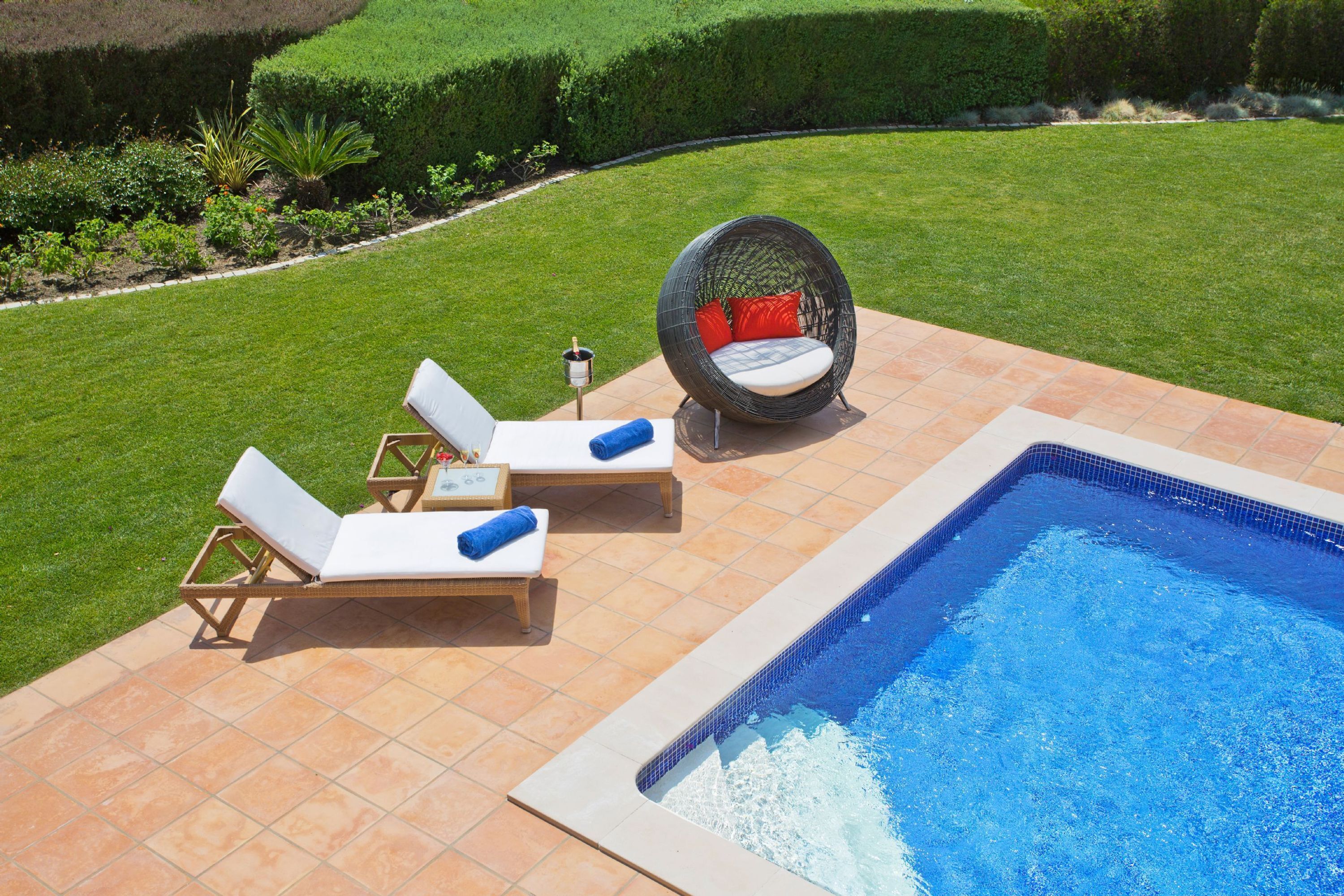 A pool area with lounge chairs and a wicker chair, surrounded by a well-manicured lawn.