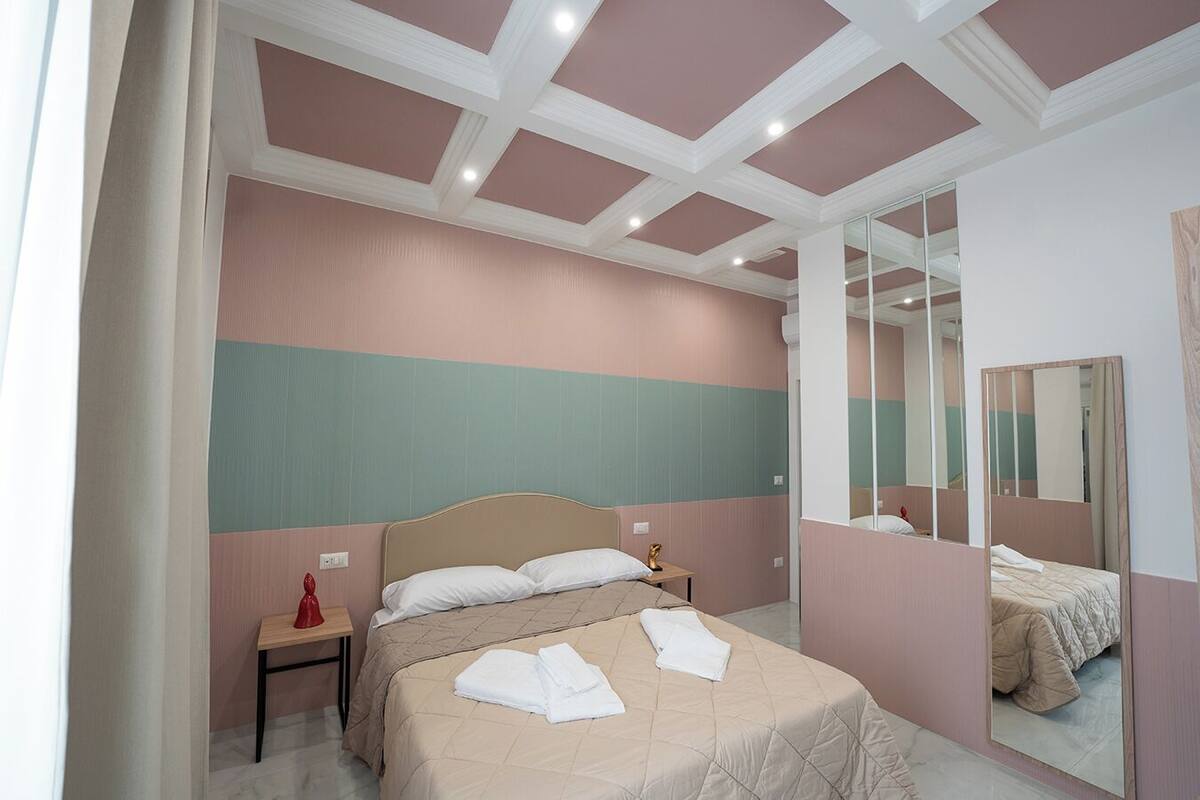 A hotel room with a bed, a nightstand, a mirror, and a wall with a geometric pattern.
