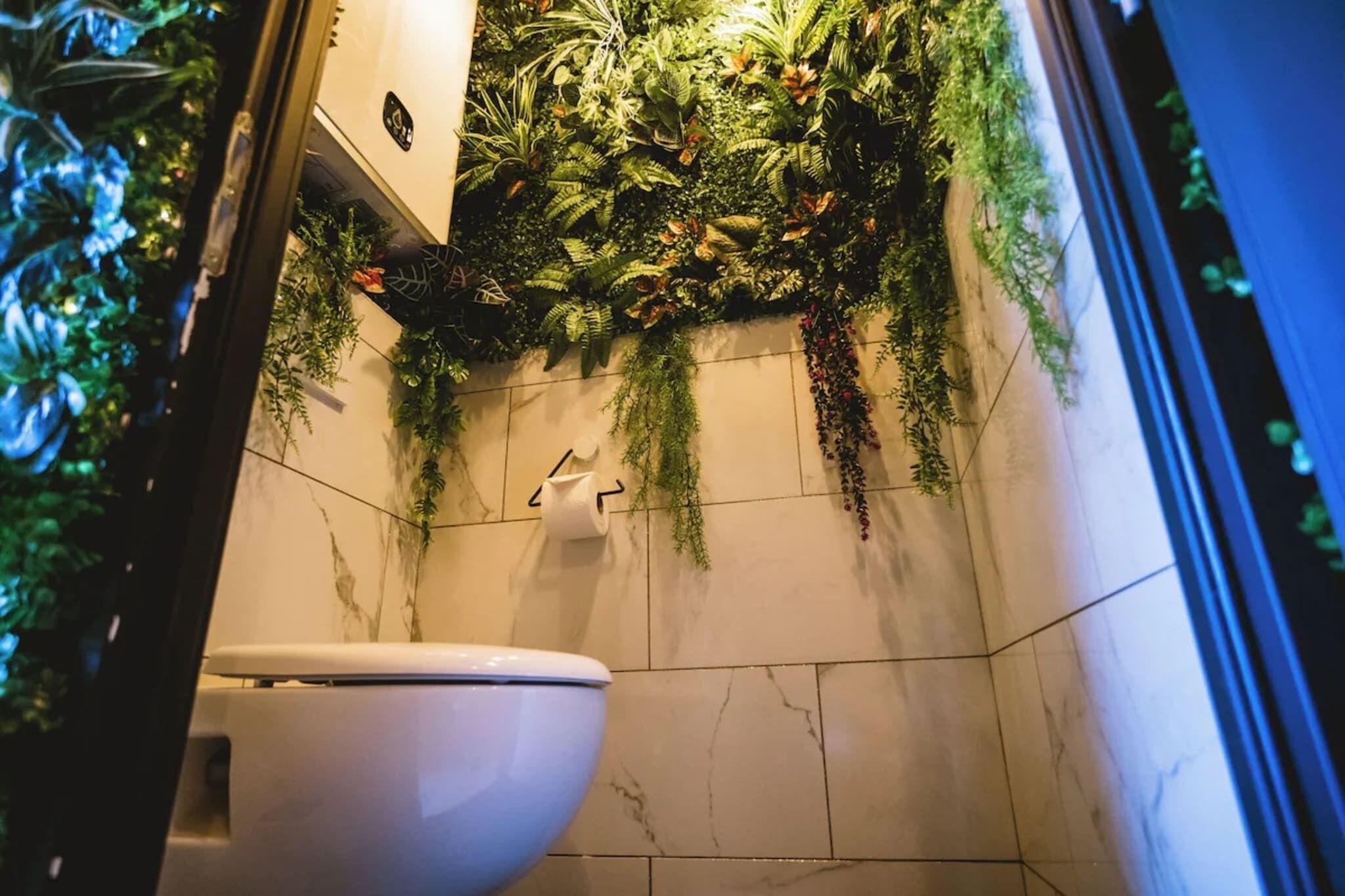 Een badkamer met een toilet, een wandfontein en een groene verticale tuin.