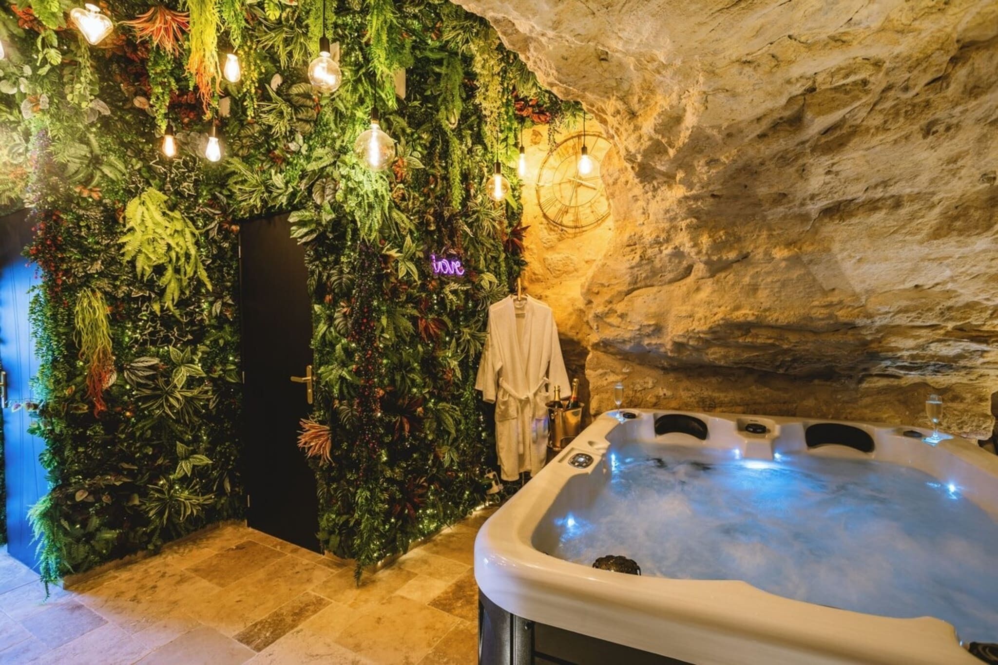 Un espace de bien-être comprenant un jacuzzi, un mur recouvert de verdure et un mur en pierre rustique.