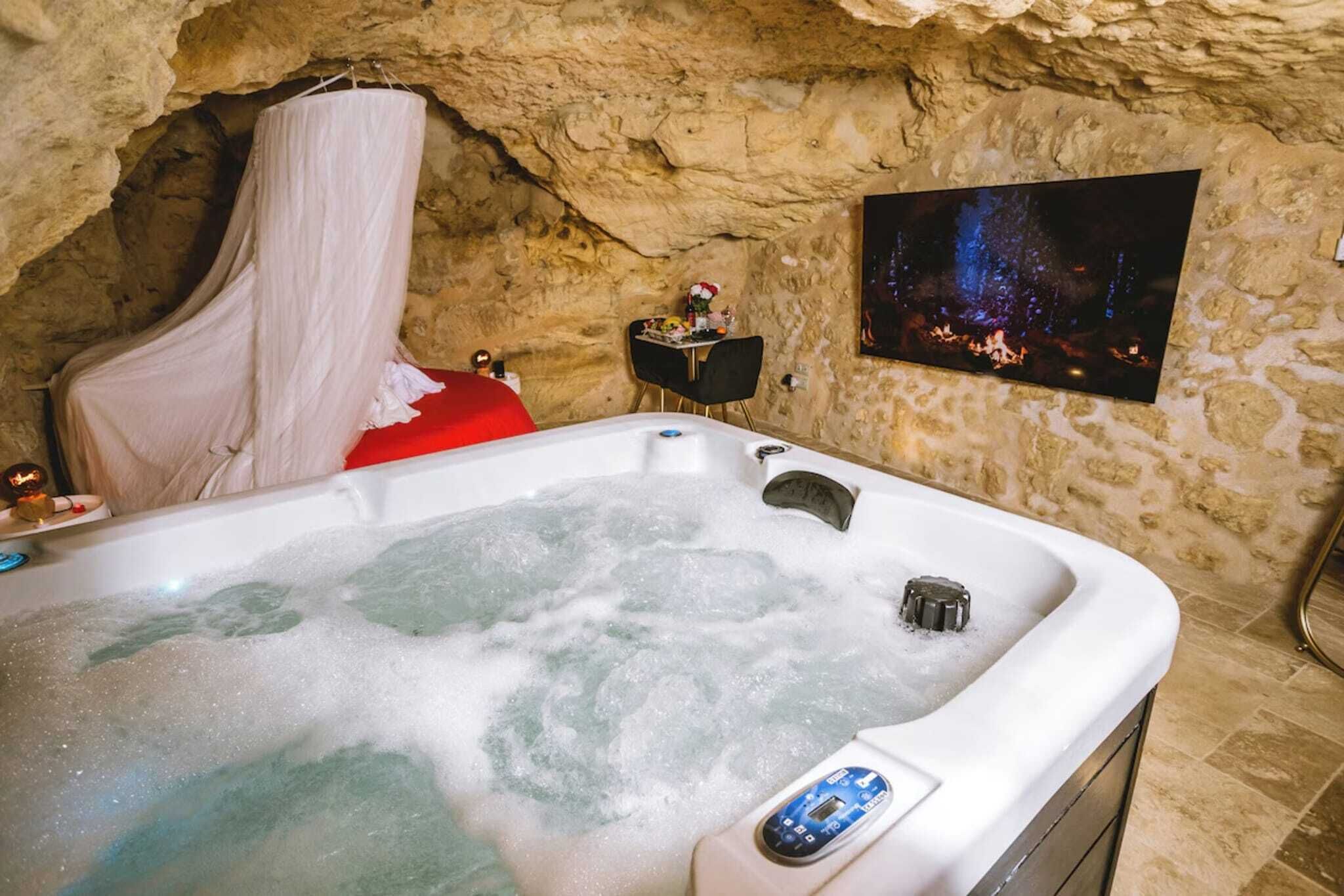 Une salle de spa avec un bain à remous, un peignoir blanc et un tableau représentant une scène de forêt accroché au mur.