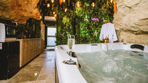 A spa area with a hot tub, a glass of champagne, and a wall decorated with greenery and lights. - La Grotte Fleurie - 5-star rating (Mussidan)