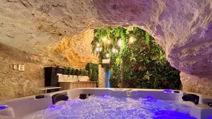 A spa area with a hot tub in a cave-like setting, surrounded by greenery and stone walls. - La Grotte Fleurie - 5-star rating (Mussidan)
