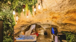 A cozy cave-like room with a bed, a hot tub, and a bar area. - La Grotte Fleurie - 5-star rating (Mussidan)