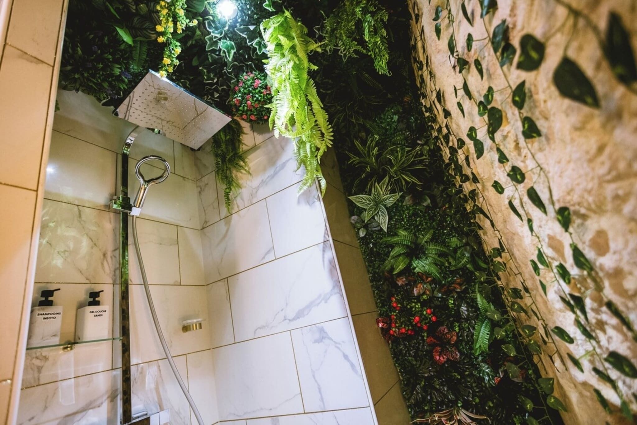 Ein Badezimmer mit Dusche, Marmorfliesen und einer Wand, die mit Pflanzen und Blumen dekoriert ist.