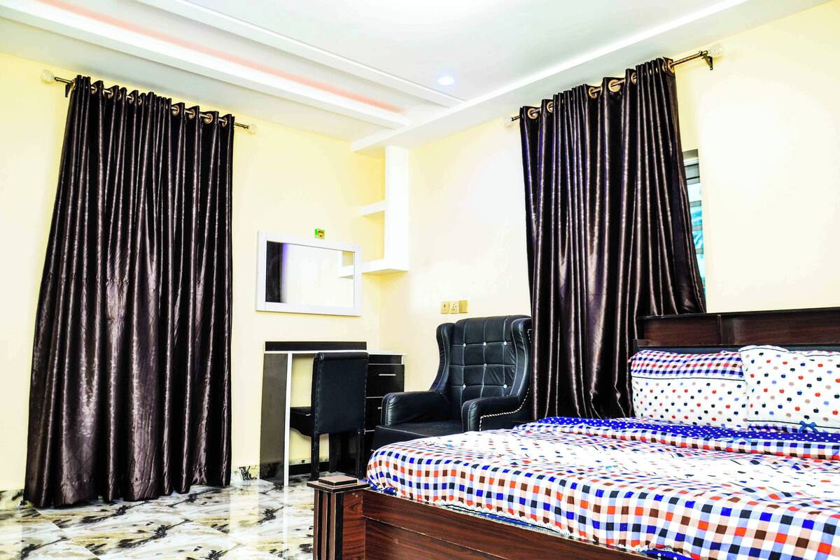 Una habitación de hotel con cama, escritorio, silla y cortinas.