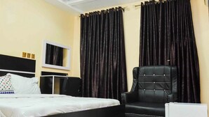 Une chambre d’hôtel avec un lit, un fauteuil en cuir noir, une télévision et des rideaux foncés.