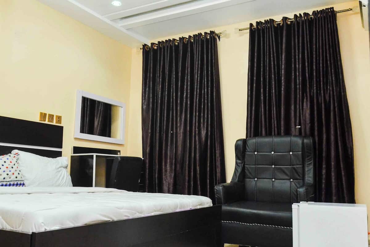 Una habitación de hotel con una cama, un sillón de cuero negro, un televisor y cortinas oscuras.
