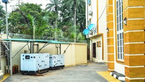 Un bâtiment à la façade jaune, doté d’un espace extérieur couvert équipé de matériel électrique et d’une antenne parabolique.