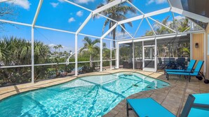 Piscina ao ar livre coberta, com água azul cristalina, rodeada por palmeiras e vista para o céu.