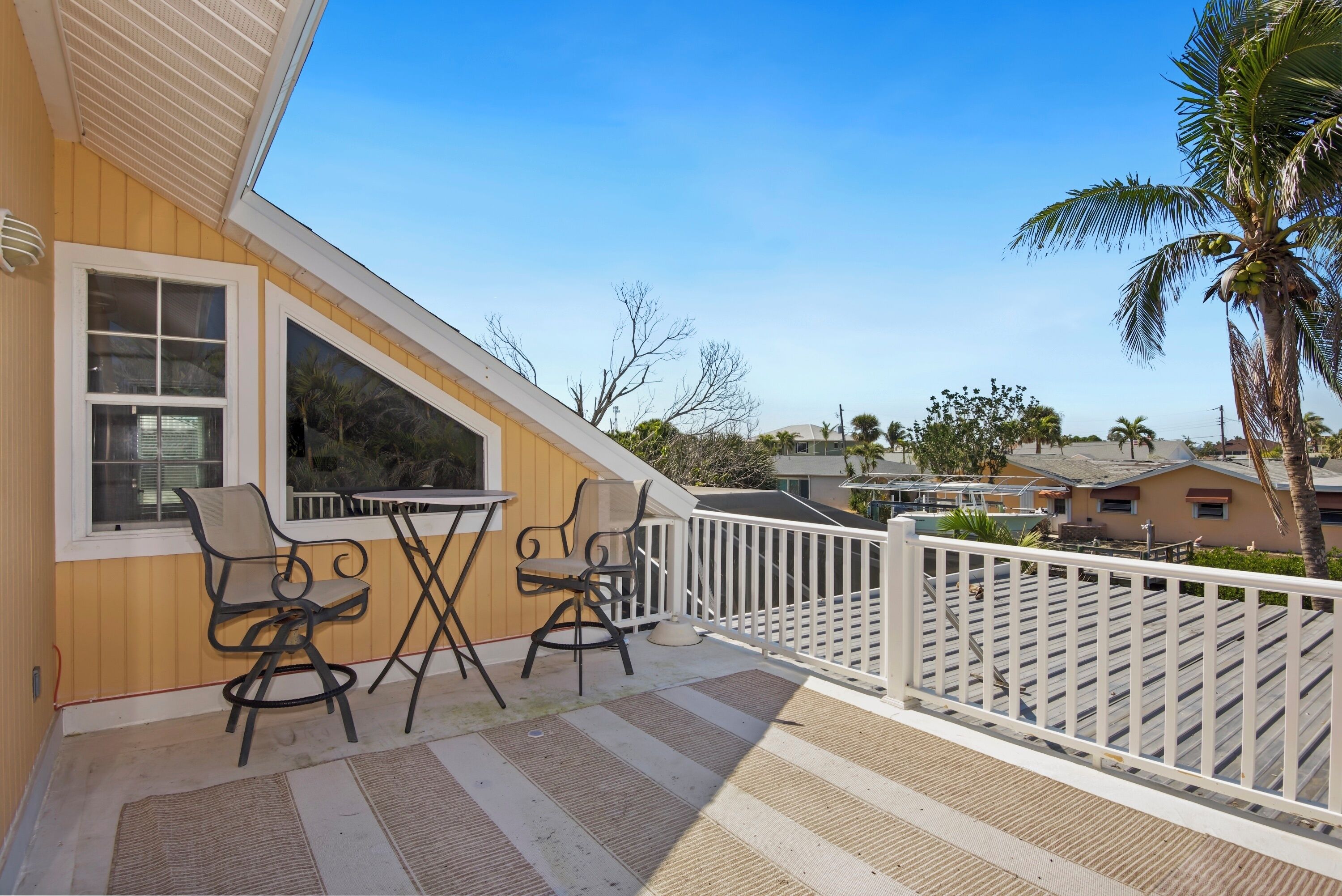 Un balcon avec une table et des chaises, une balustrade blanche et une vue sur des palmiers et des maisons.