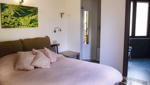 A bedroom with a large bed, a painting on the wall, a small bedside table, and a door leading to another room. - Double Room. The Garden. Rooms & Breakfast. (La Maddalena)