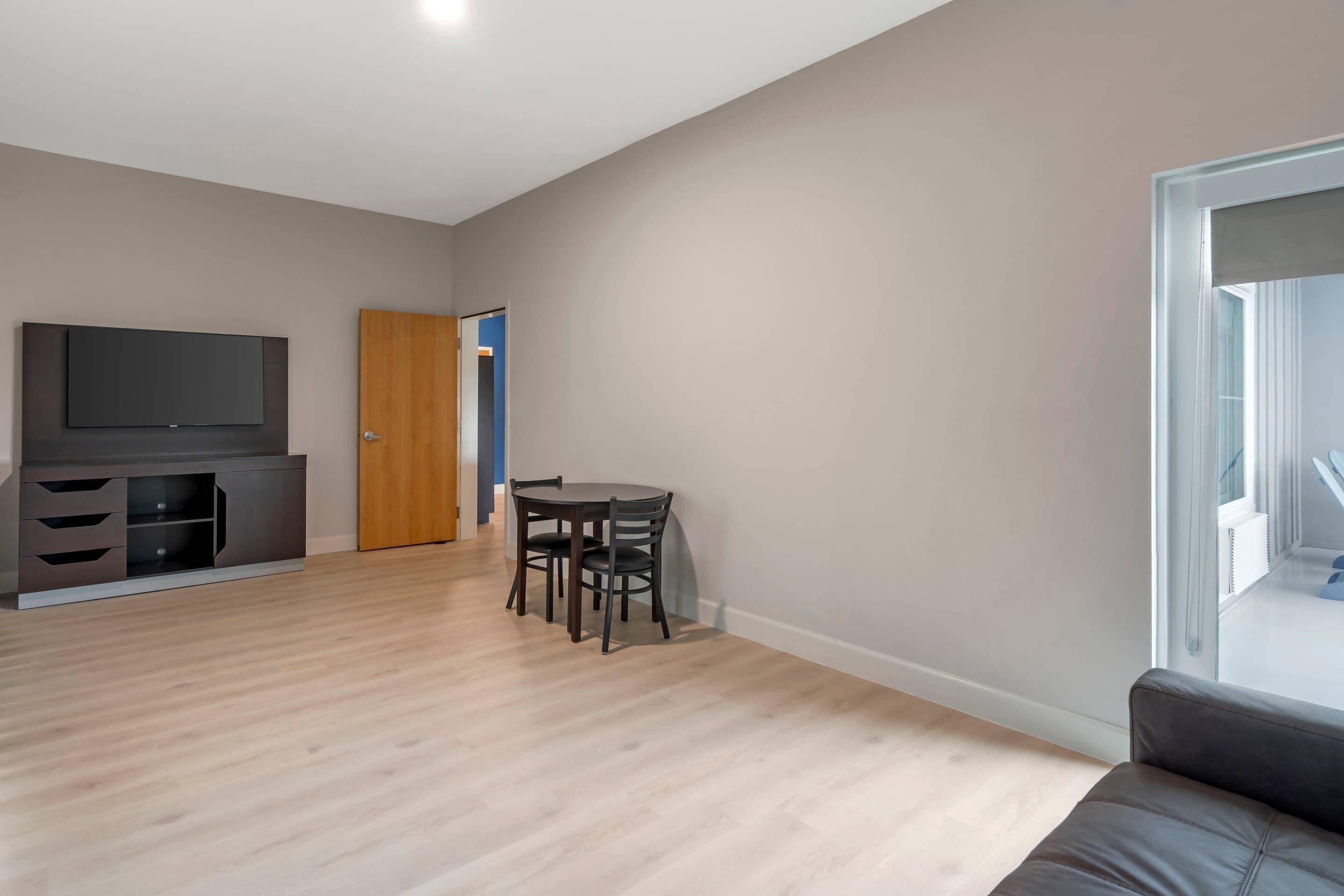 A modern living room with a flat-screen TV, a dining table with chairs, a sofa, and a wooden door.