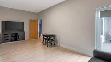 A modern living room with a flat-screen TV, a dining table with chairs, a sofa, and a wooden door.