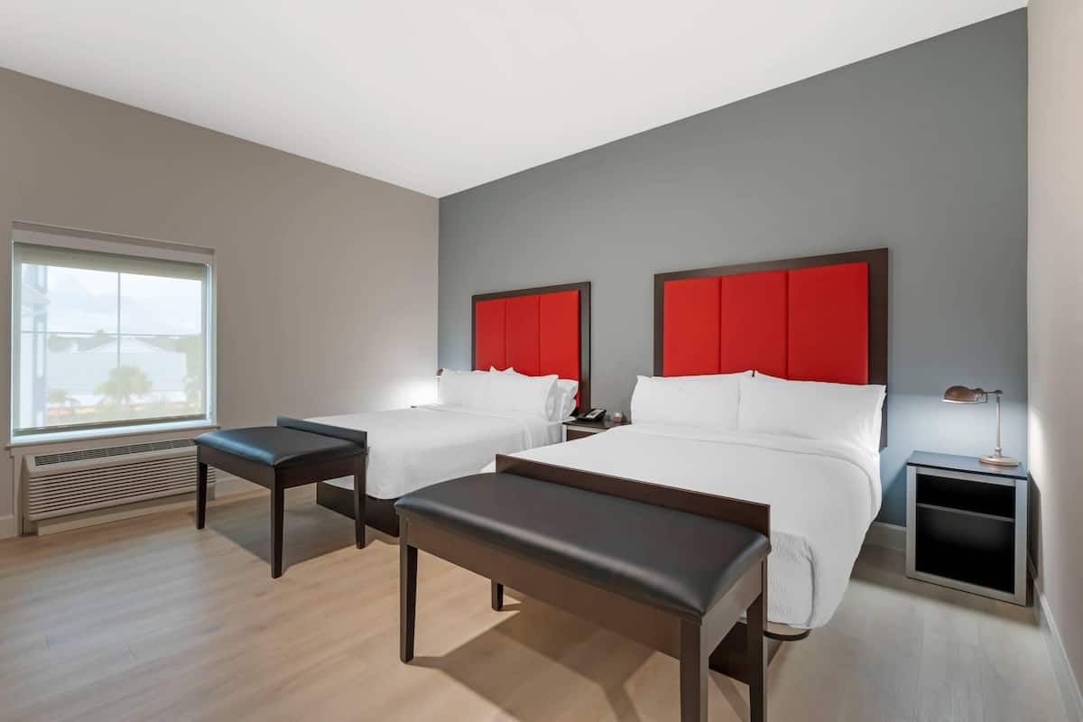 Een hotelkamer met twee bedden, een bankje, een nachtkastje en een raam met jaloezieën.