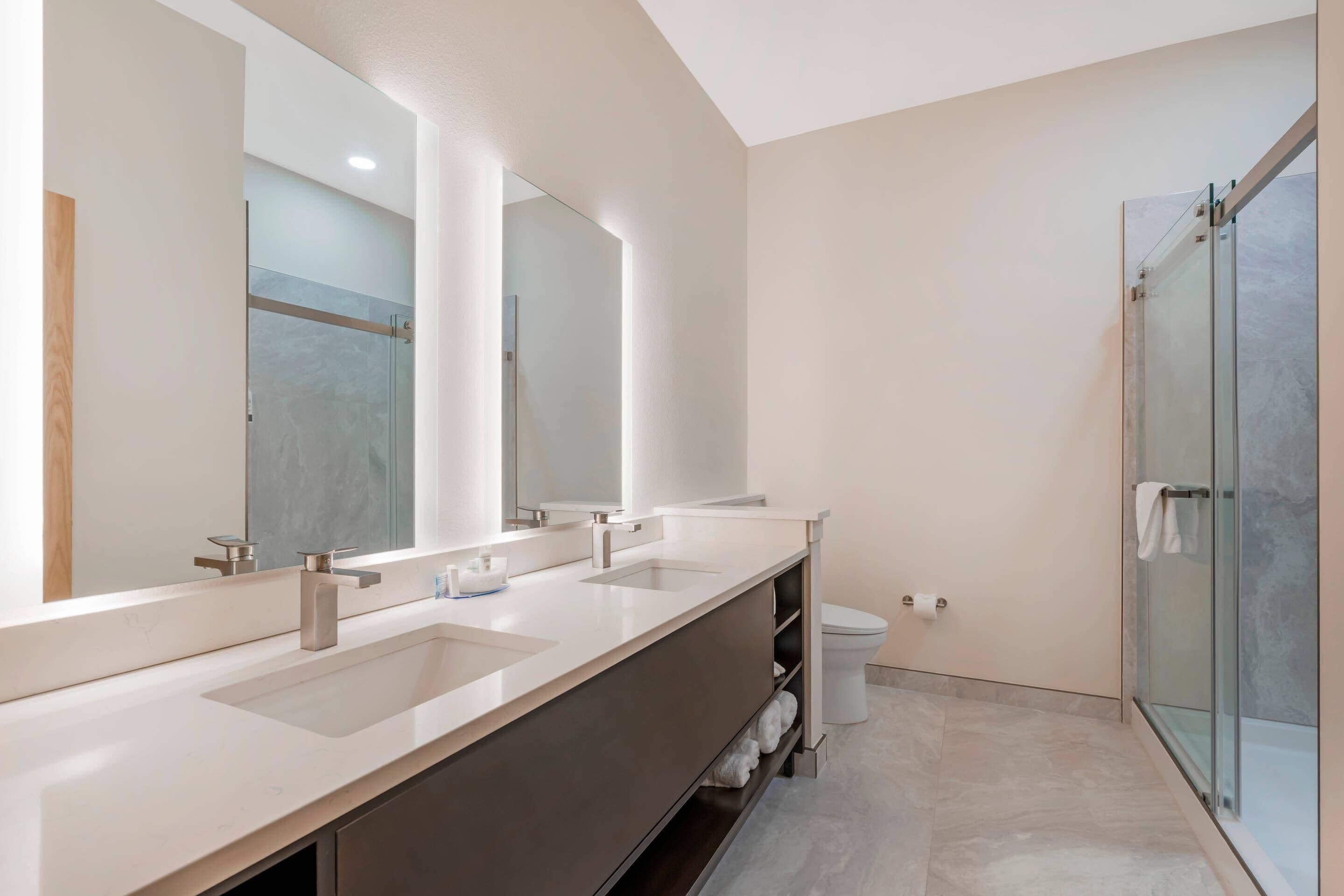 Un baño moderno con un tocador amplio, dos lavamanos, cabina de ducha de vidrio y un inodoro.