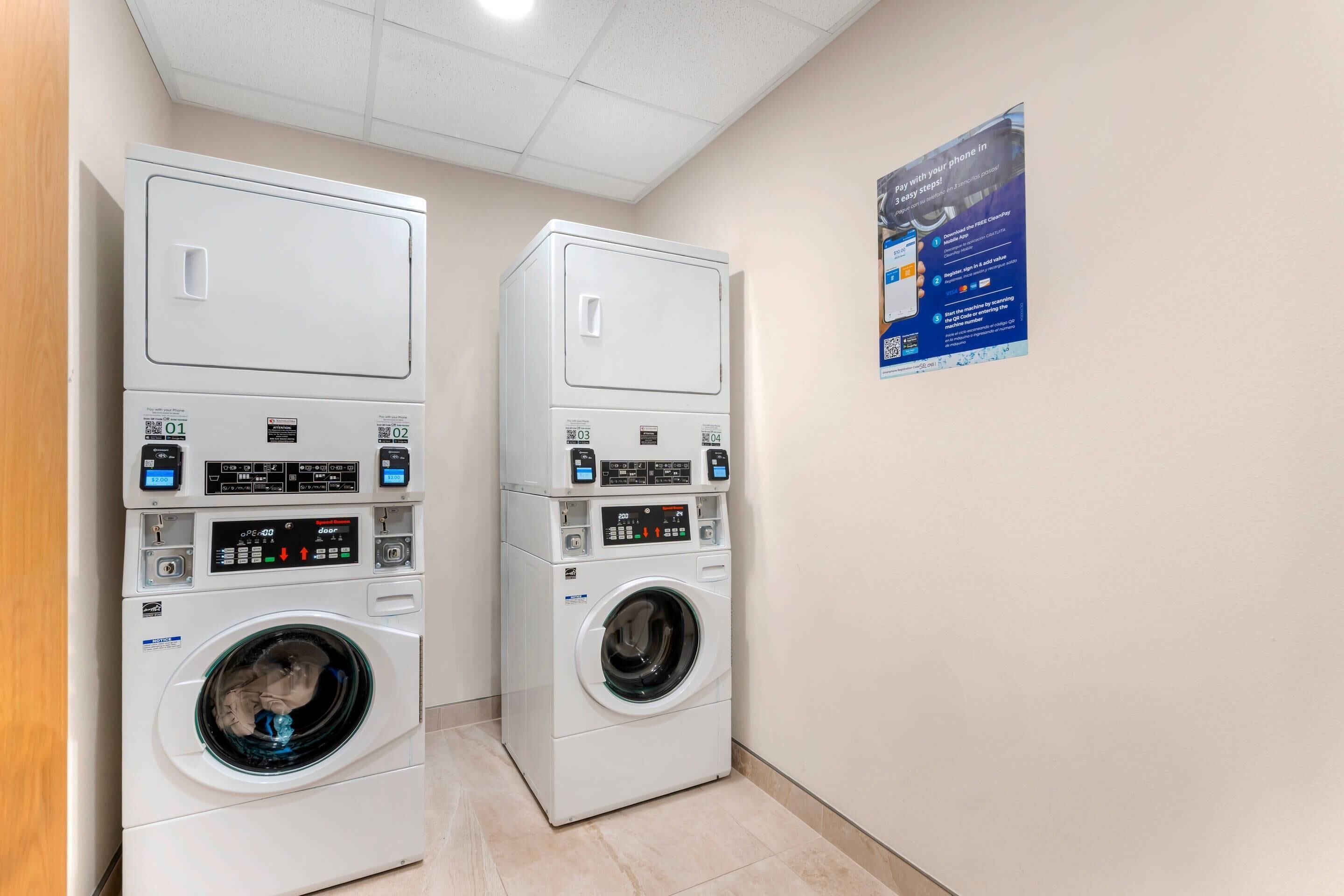 Two stacked front-loading washing machines in a hallway with a poster on the wall.