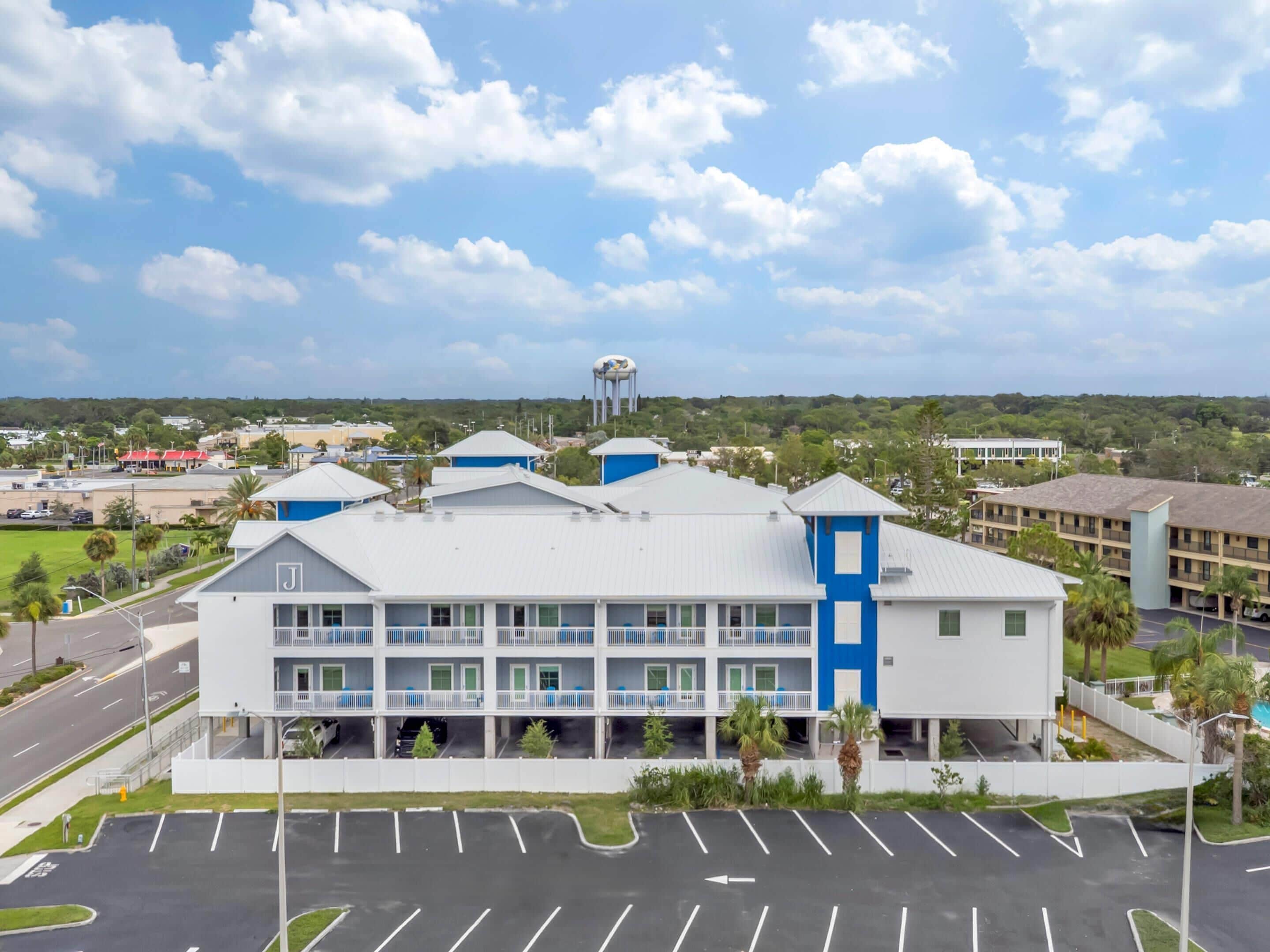 A multi-story hotel with a parking lot in front, a water tower in the background, and a clear sky.