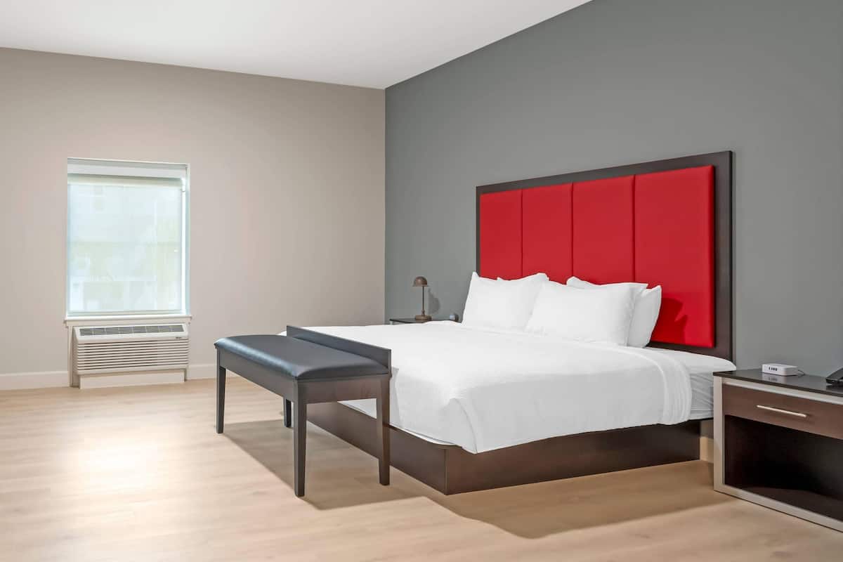 Een moderne hotelkamer met een groot bed, een nachtkastje, een bankje en een raam met zonwering.