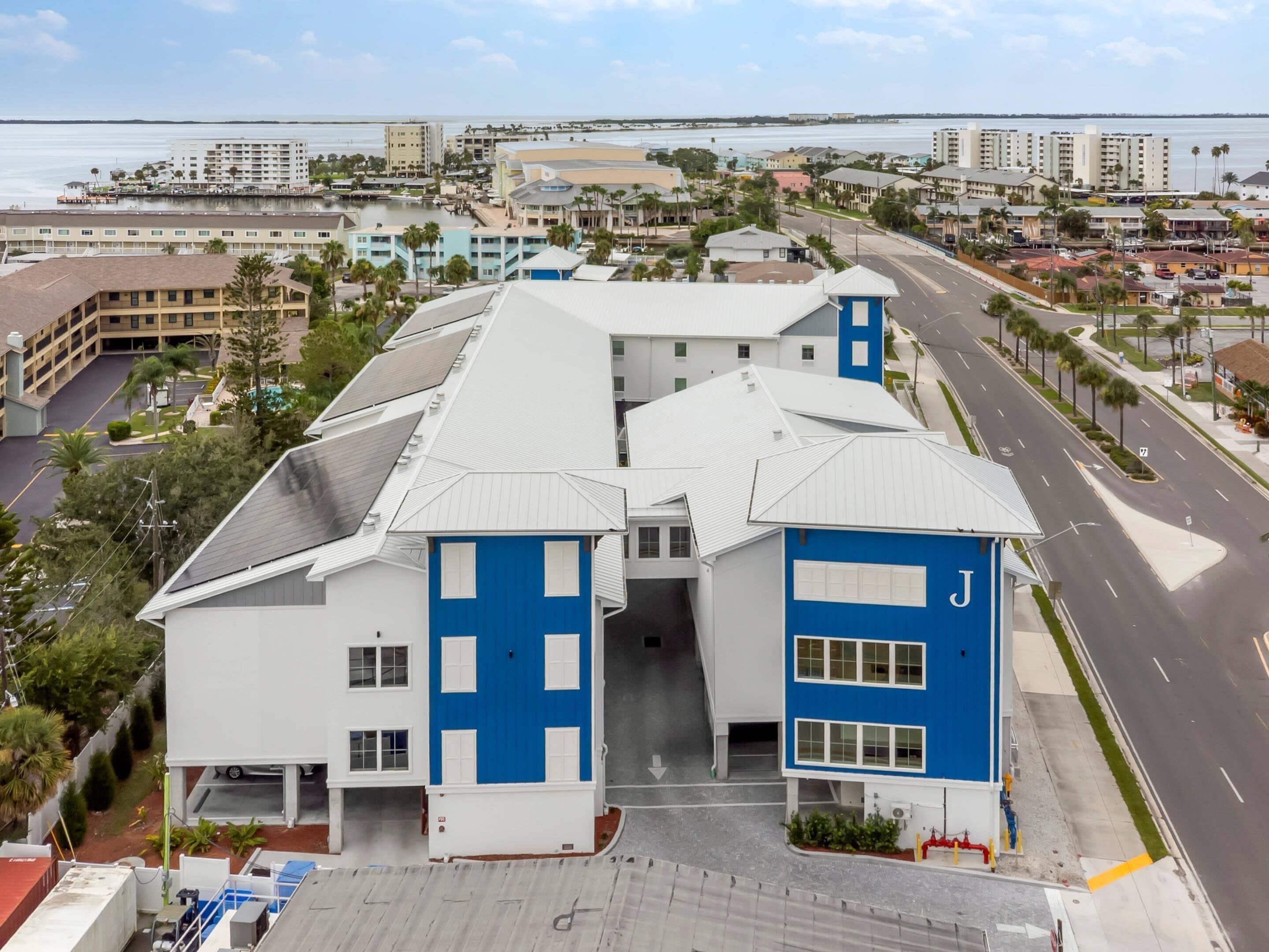 Un hotel de varios pisos con una fachada destacada en azul y blanco, una entrada central y vistas del área urbana circundante y la costa.