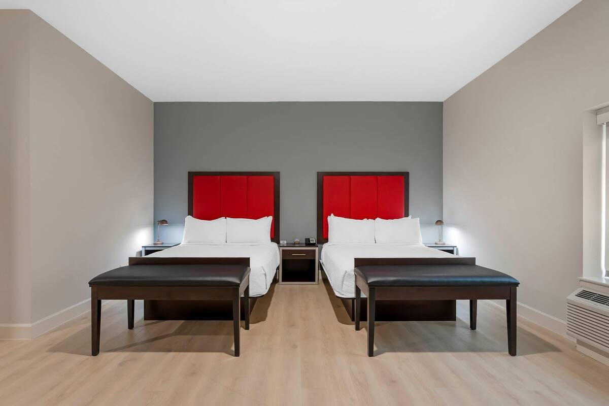 Een hotelkamer met twee bedden, een rode hoofdbord, nachtkastjes en een raam.