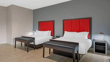 A hotel room with two beds, a desk, a chair, a nightstand, and a lamp.