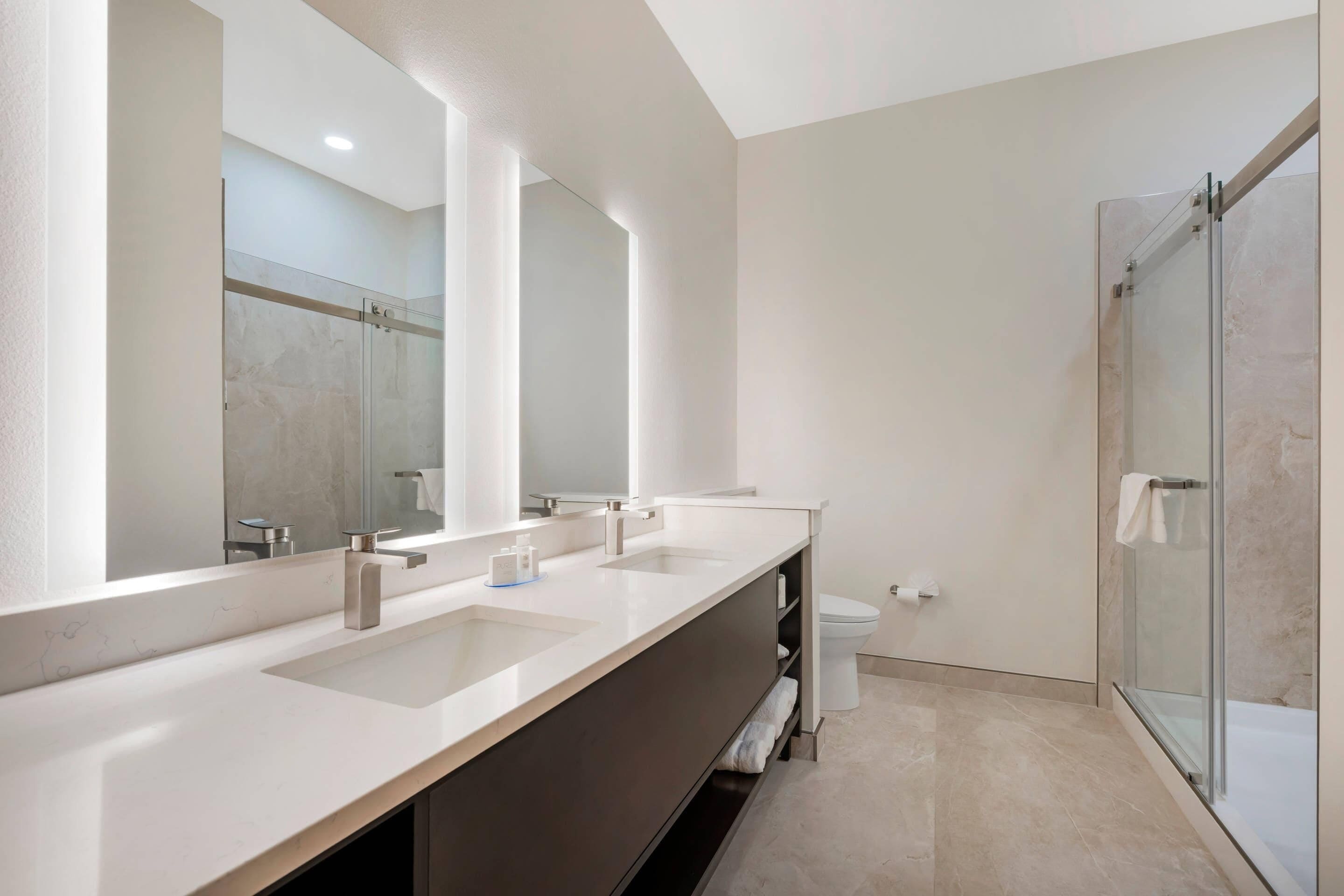 Een moderne badkamer met een lange wastafel, een douchecabine van glas en een toilet.