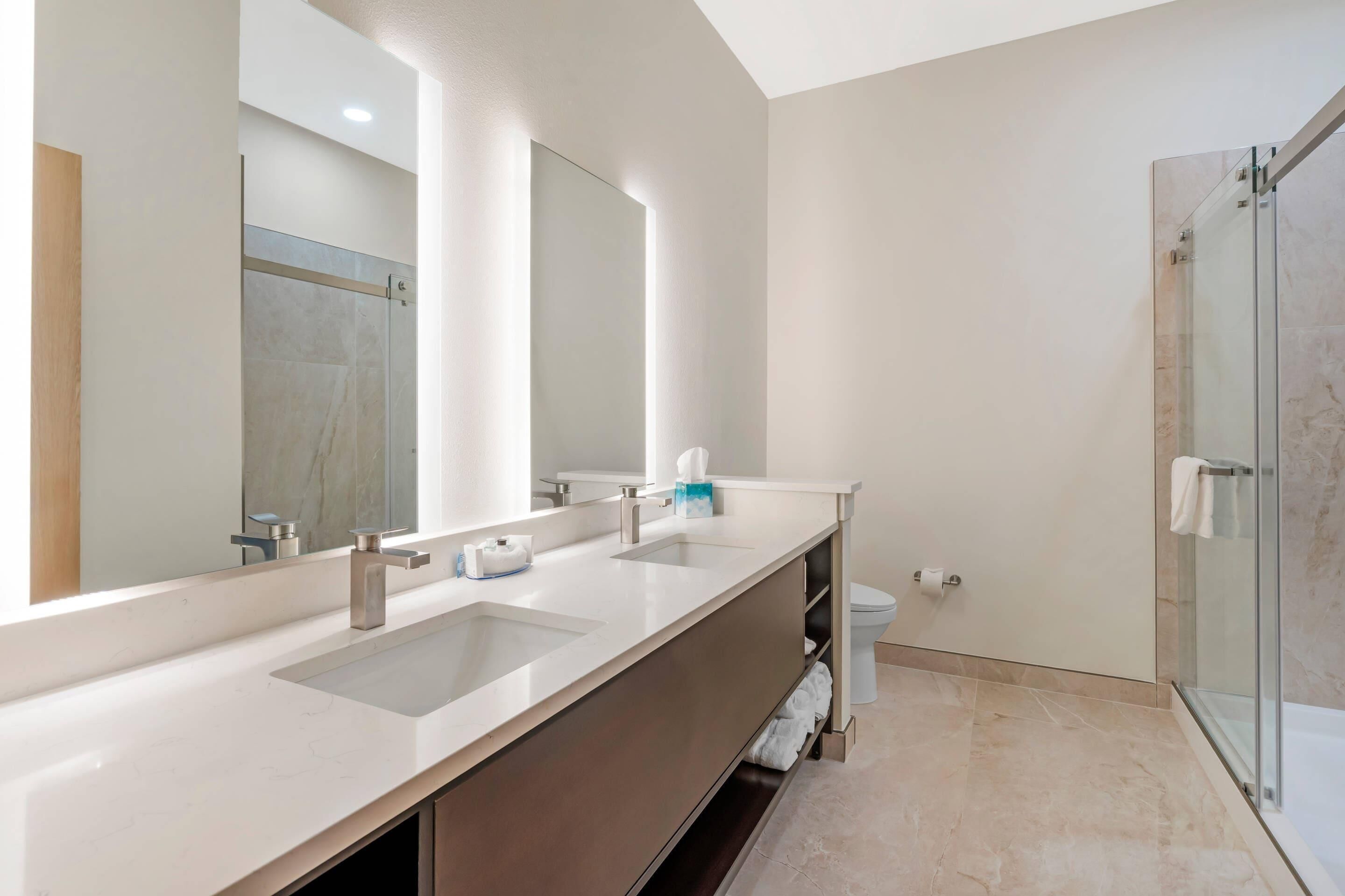 Un baño moderno con un espejo grande, dos lavamanos, ducha y un inodoro.