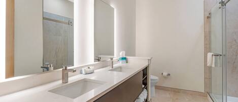 Un baño moderno con un espejo grande, dos lavamanos, ducha y un inodoro.