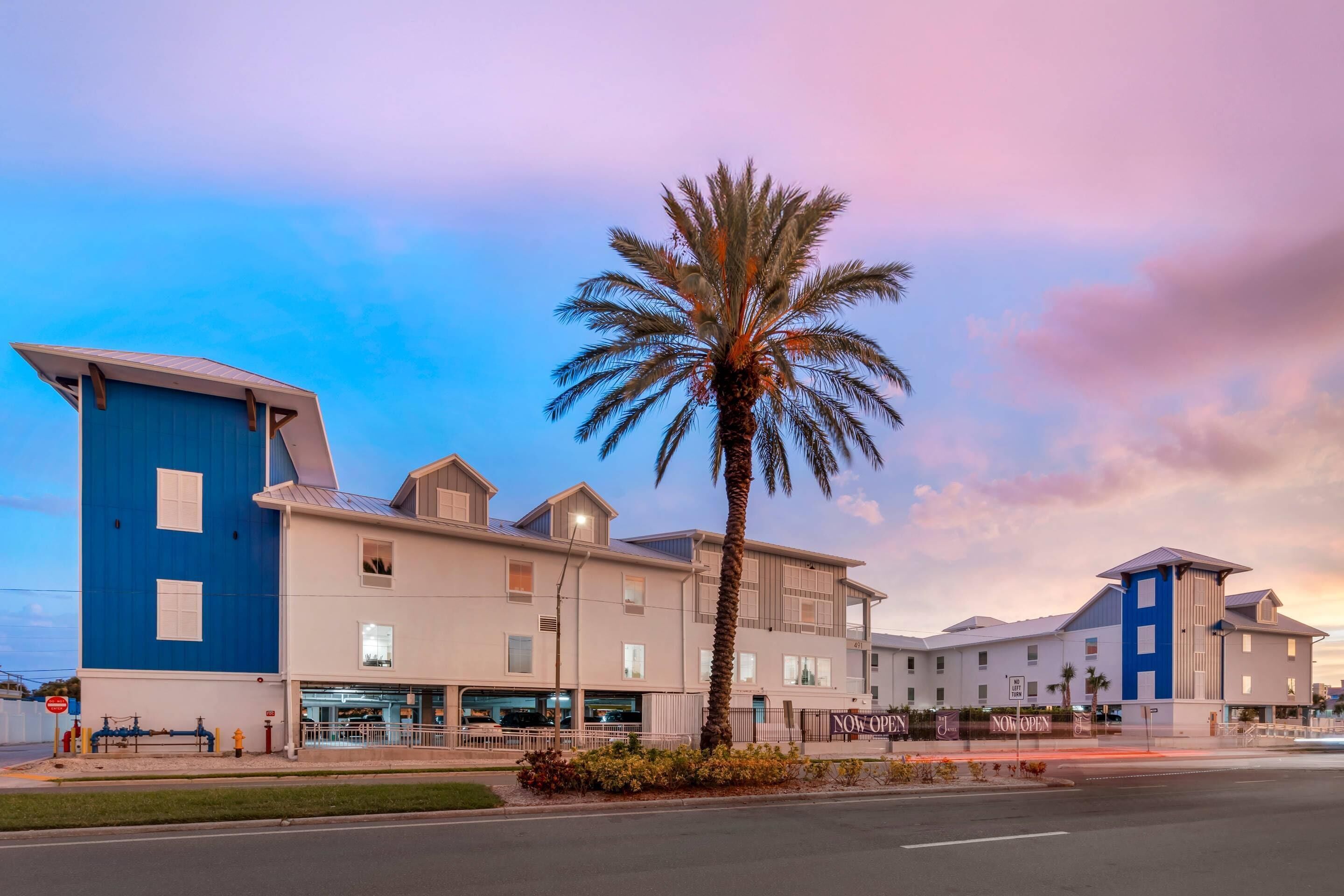 A hotel with a blue and white exterior, a palm tree in front, and a clear sky.