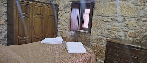 Ein Zimmer mit einem Bett, zwei Handtüchern, einem Holzschrank, einer Steinsäule und einem Fenster.