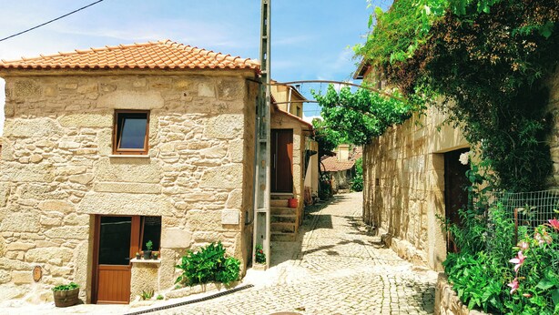 A stone building with a tiled roof, a narrow cobblestone street, and greenery growing on the walls. - Village of Moura Morta (Castro Daire)