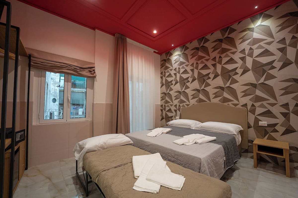 Une chambre d’hôtel avec deux lits, une fenêtre donnant sur un paysage agréable, un mur orné d’un motif géométrique et un plafond rouge.