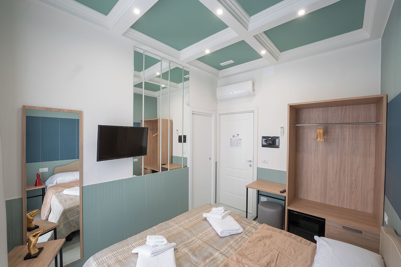 A hotel room with a bed, a TV, a wardrobe, a mirror, and a small table.