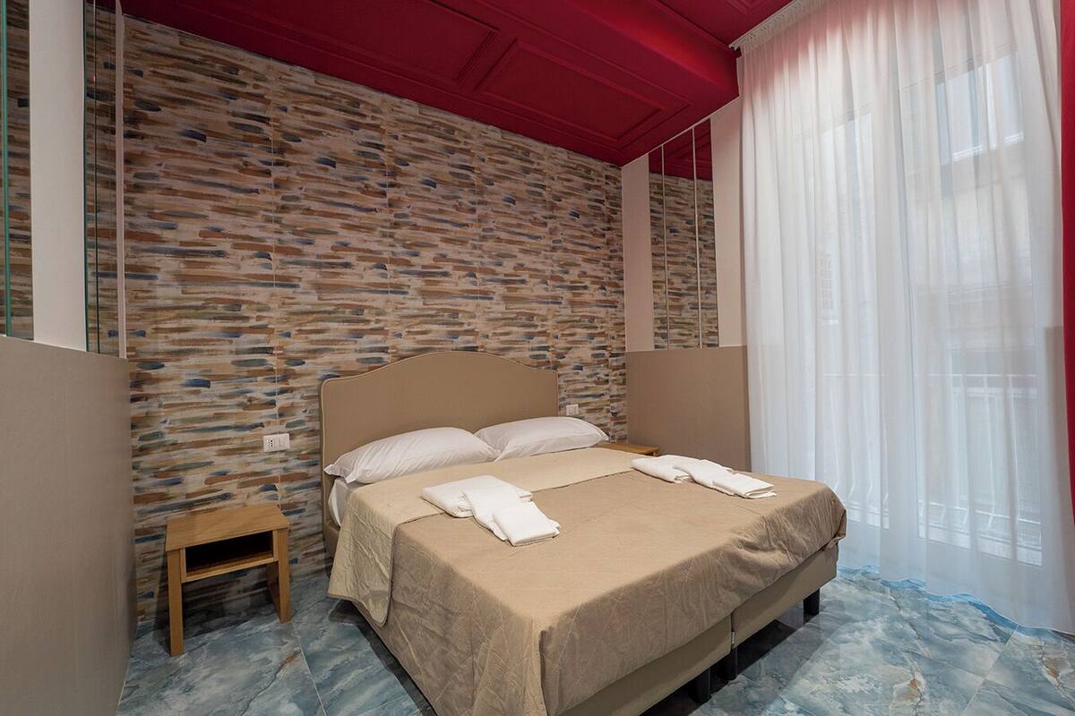 Une chambre avec un mur décoré d’un motif en pierre, une tête de lit en bois, une table de chevet et un lit avec du linge de lit et des serviettes blancs.