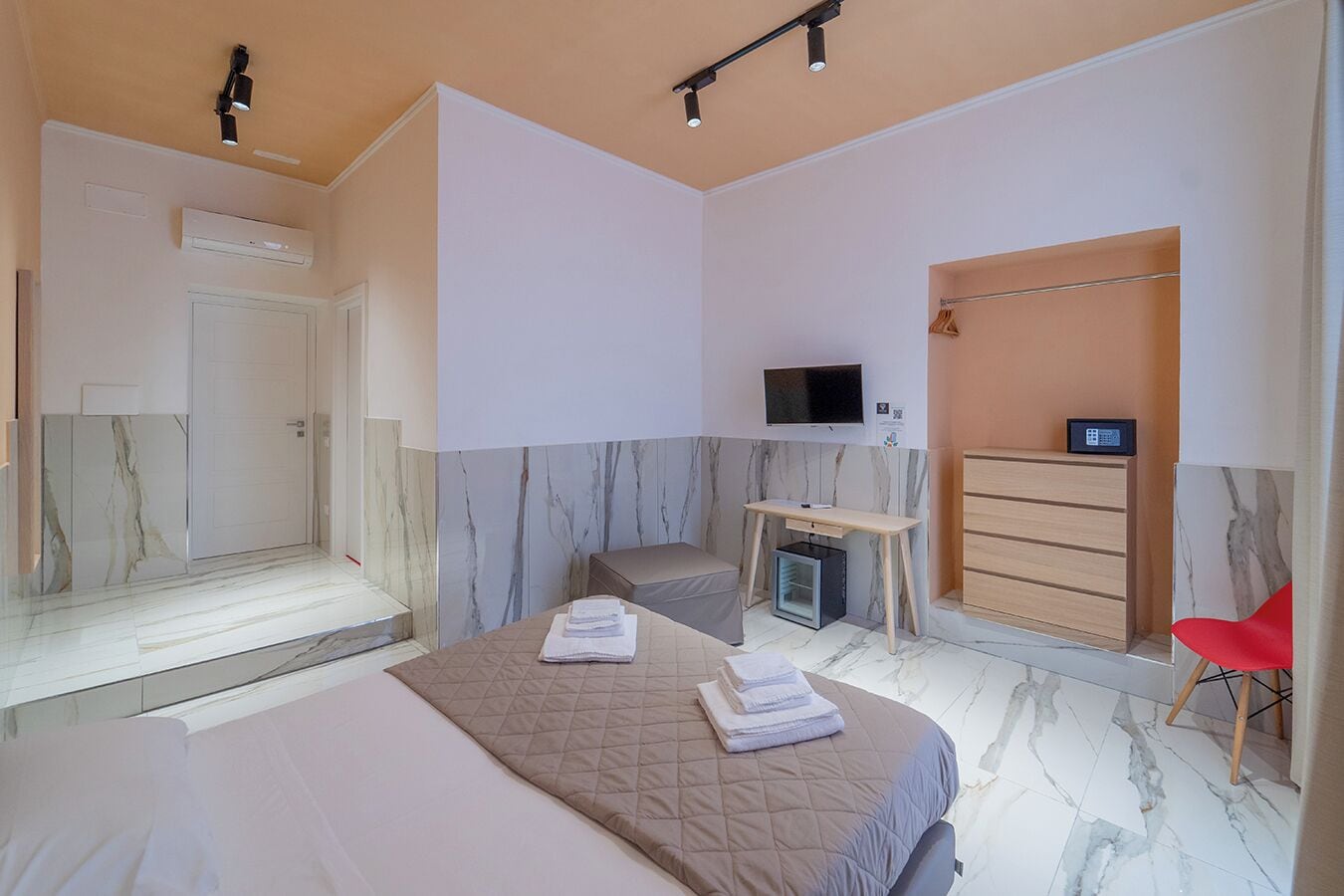 A hotel room with a bed, a desk, a TV, a wardrobe, and a red chair.