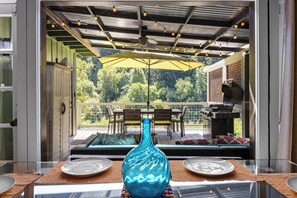 Ein Essbereich mit Tisch, Stühlen, einem gelben Sonnenschirm und einer blauen Vase.
