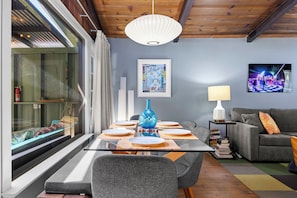 Ein moderner Essbereich mit einem Glastisch, grauen Stühlen, einer blauen Vase und einem grauen Sofa.