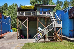 A multi-level wooden structure with a balcony, a covered area with an umbrella, and a view of the surrounding forest.