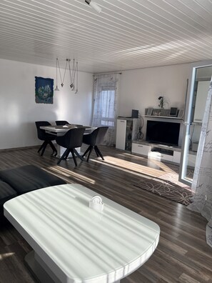A modern living room with a dining area, a flat-screen TV, and a sofa. - Vacation apartment Klenk - 3 (Ostfildern)