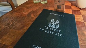 Un livret d’accueil noir intitulé « LA FERME DU CERF BLEU », comportant un code QR, ainsi qu’un bloc de bois également doté d’un code QR.