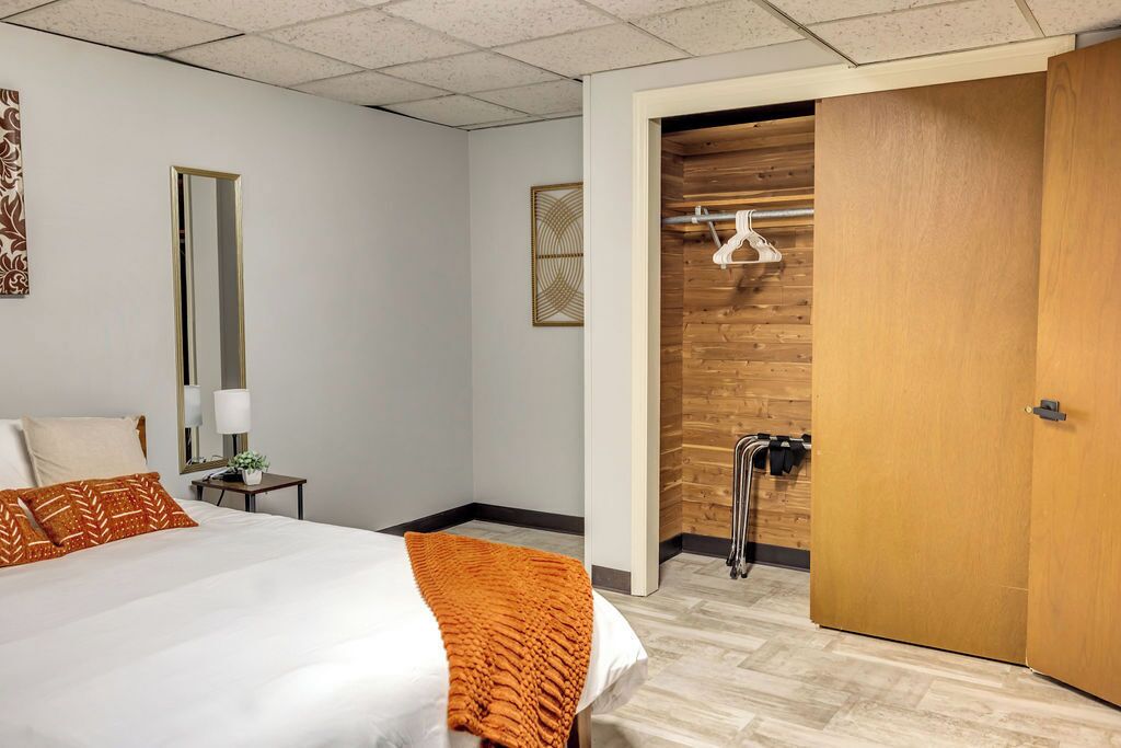 A hotel room with a bed, a nightstand, a mirror, a wooden wall, and a door.